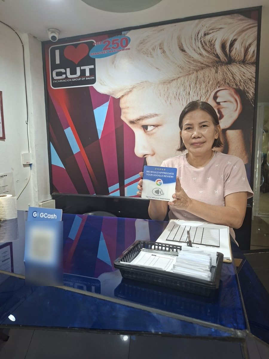 A staff member at I ♥ Cut Salon holds their Tap It Google review card at the front desk.