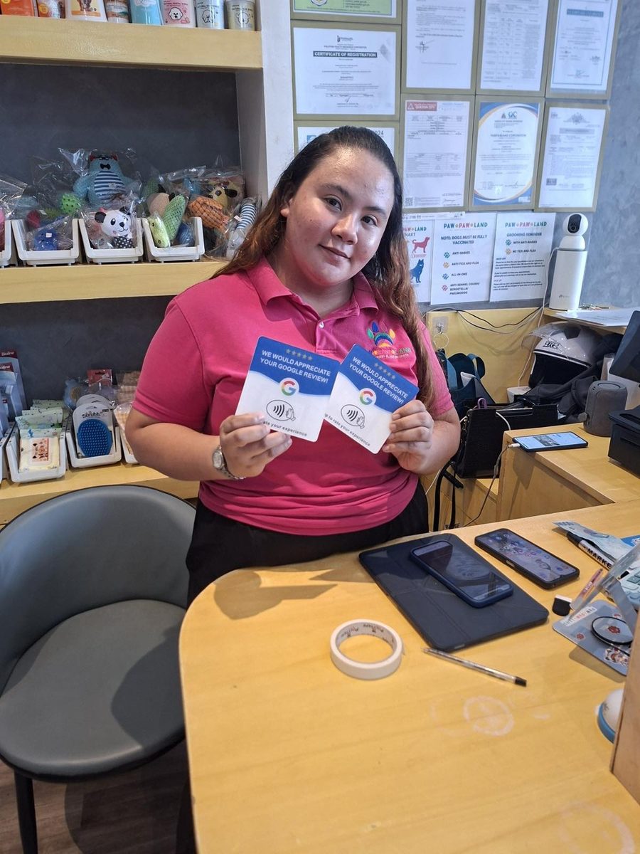 A Paw Paw Land staff member holds two Tap It Google review cards at the shop counter.